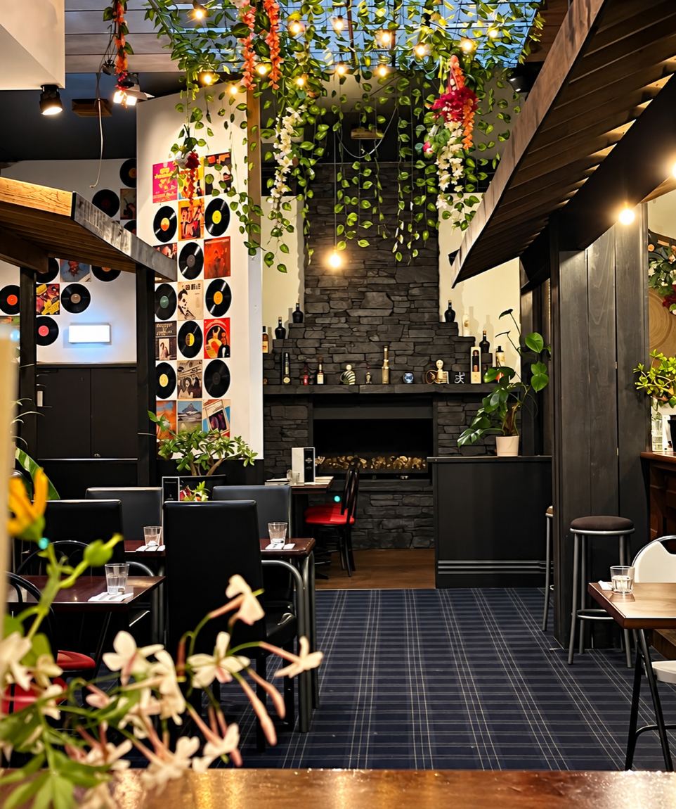 The dining room at Mia Kusina — record sleeves across the wall, greenery and lights hanging from the skylight, a stone fireplace at the back.
