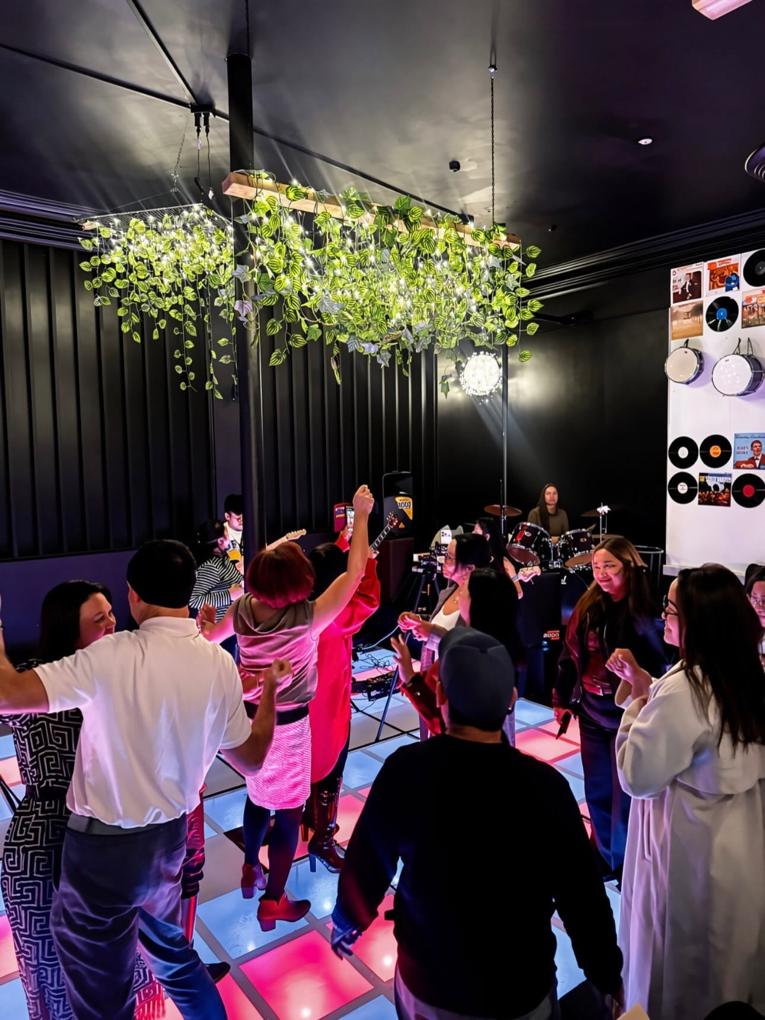 A crowd dancing on the lit floor at Mia Kusina while a band plays under the hanging greenery.