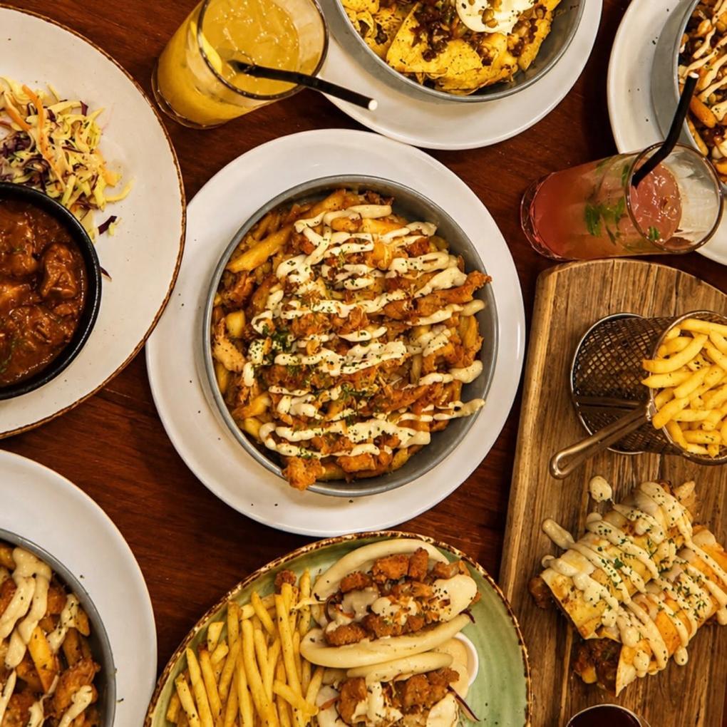 Several bowls of loaded fries, bao and curry across a dark wooden table.