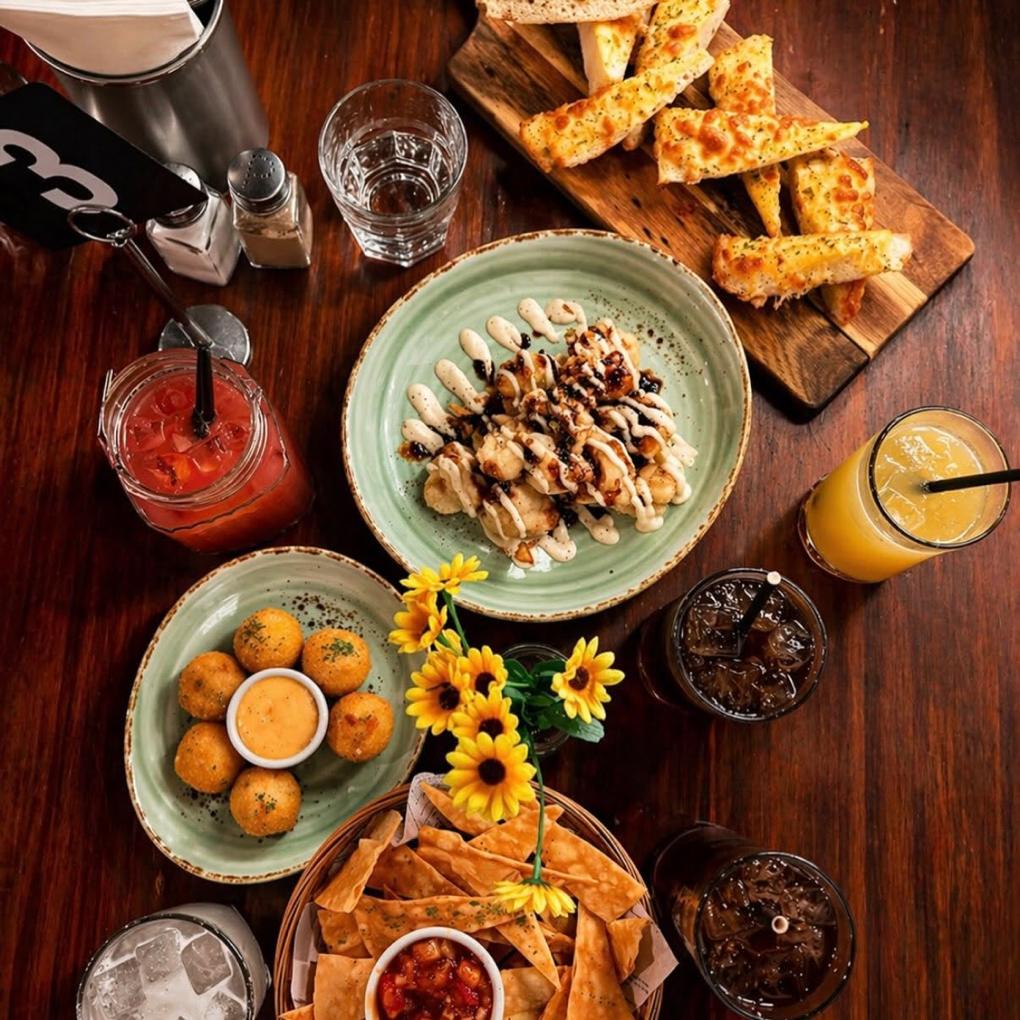 Cheesy garlic bread on a board, adobo cauliflower, cheese balls and chips with salsa on a dark table.